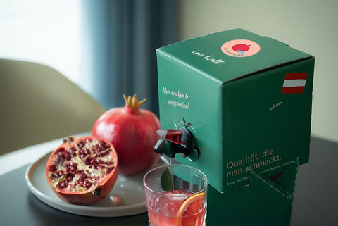 Foto der MySyrupBox Granatapfel Sirup Light auf einem Tisch mit einem Glas und Granatäpfel auf einem Teller